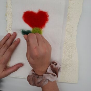 Feutrage à l'aiguille d'un cœur sur une pièce de feutre avec de la laine colorée. 