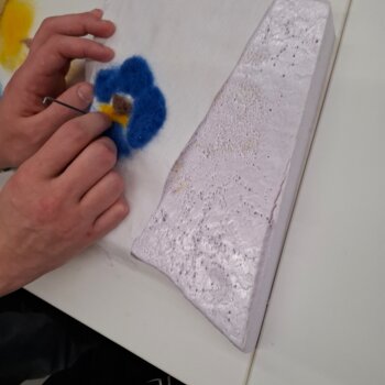 Feutrage à l'aiguille d'une fleur bleue sur une pièce de feutre.