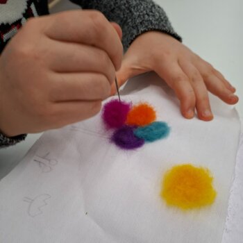 Une personne utilise une aiguille à feutrer pour piquer de la laine colorées (rose, orange, turquoise, violet et jaune) sur un tissu blanc, une technique appelée feutrage à l'aiguille.