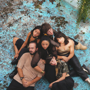 Photographie vue d'en haut du groupe Las Baklavas. Le groupe a les yeux fermés, assis au sol et regroupés les uns contre les autres.