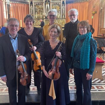 Cette image montre six musiciens souriants posant avec leurs violon dans une église au sol carrelé de motifs géométriques