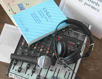 Une table de mixage audio, équipée d'un microphone et d'un casque, est posée à côté de plusieurs livres, dont un ouvrage intitulé « Grâce... Livre des heures poétiques »