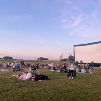 Ciné plein air avec un coucher de soleil, serviettes installés sur une pelouse