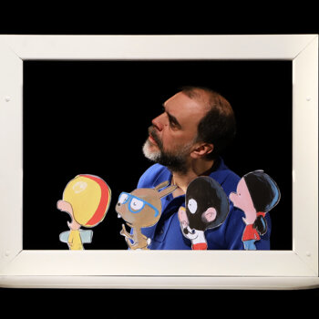 Un homme derrière un cadre théâtral manipule quatre personnages en carton colorés sur fond noir.