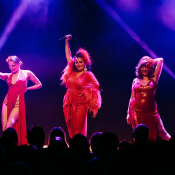 Trois femmes en tenues de scène rouges effectuent une performance devant un public.